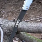 Close-up of a folding saw cutting through a tree branch.