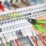 Hand using wire cutters on electrical panel with colorful wires.